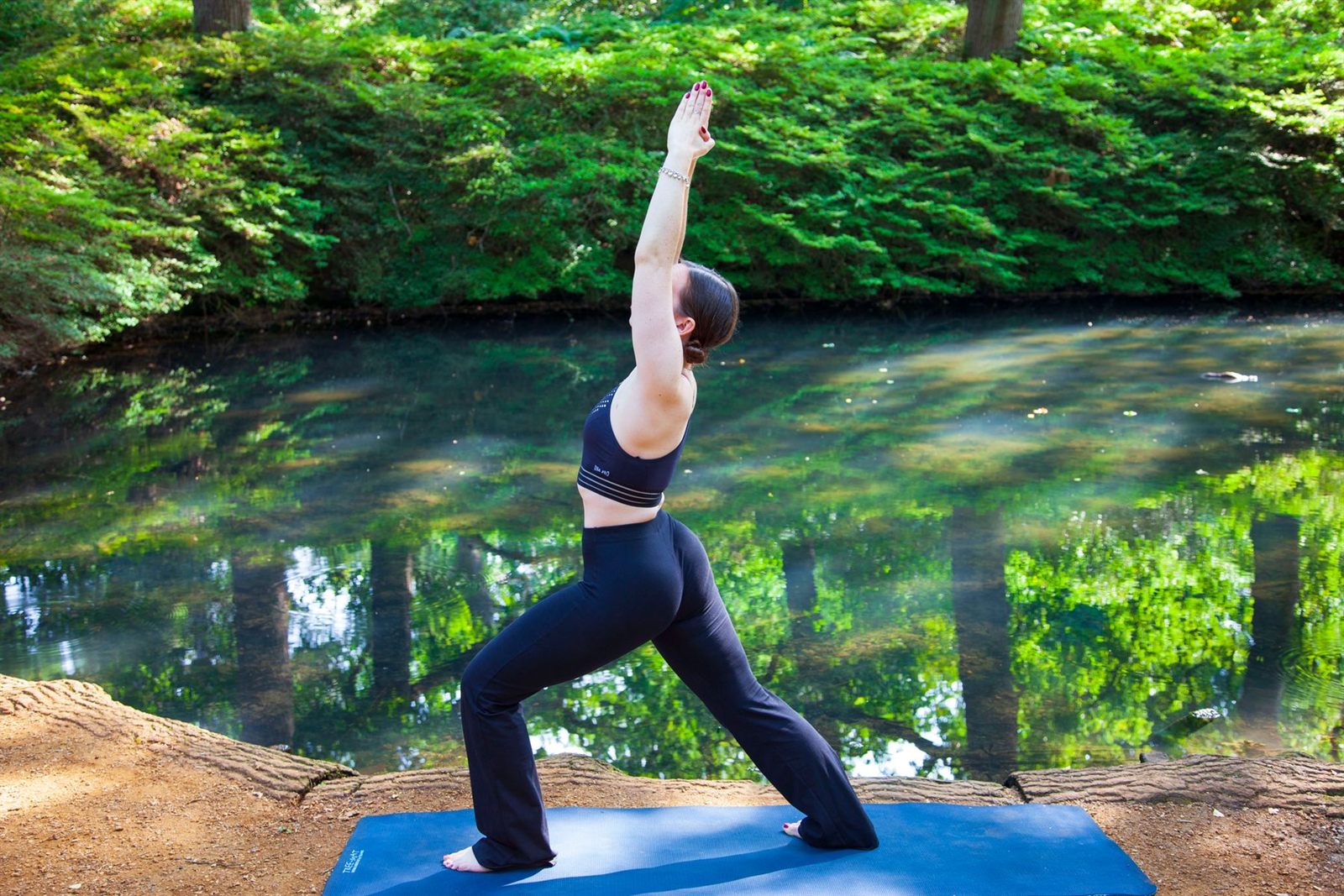 Orman gölünün kıyısında savaşçı pozunda yoga yapan kadın